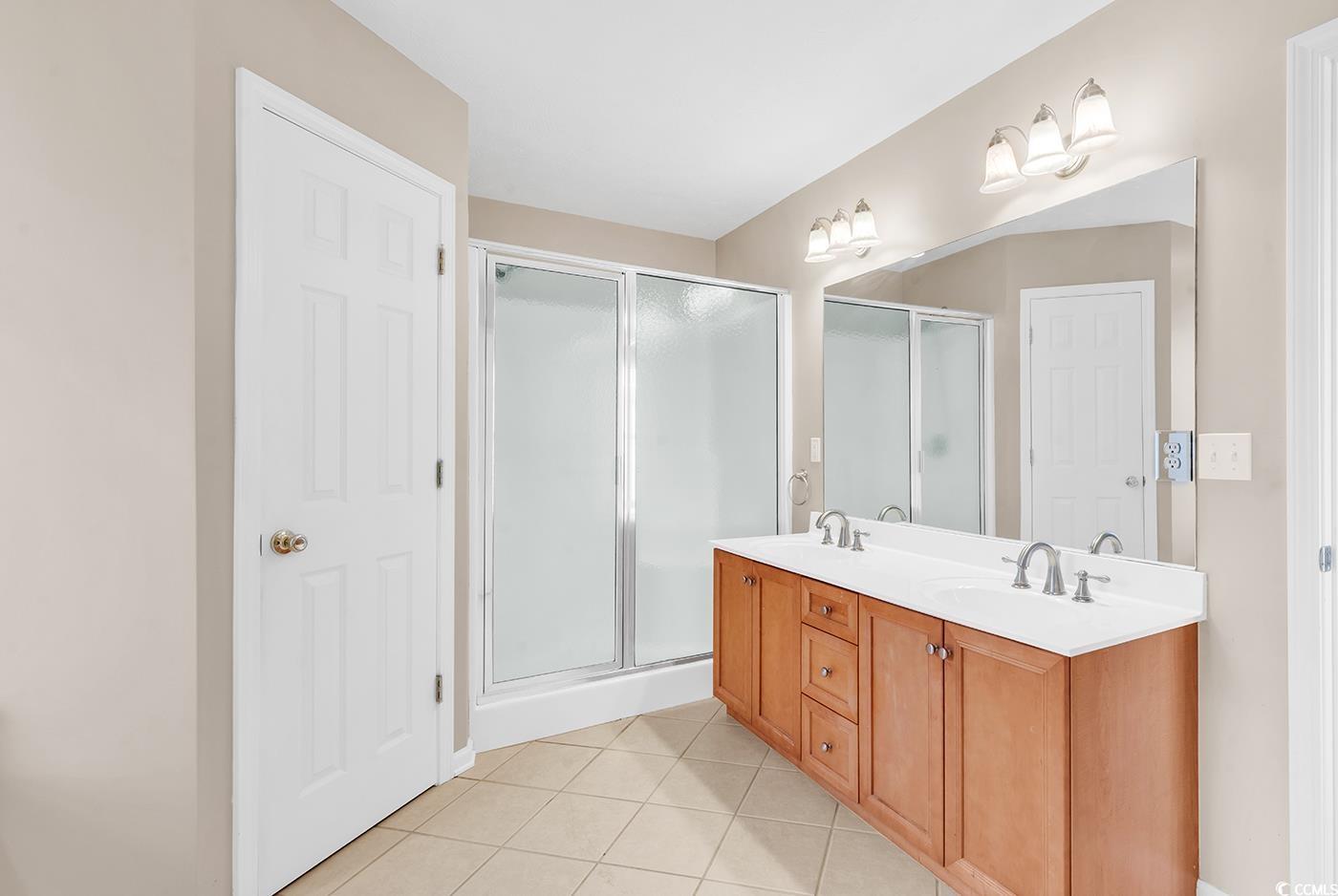Full bath featuring light tile patterned floors, a stall shower, and double vanity