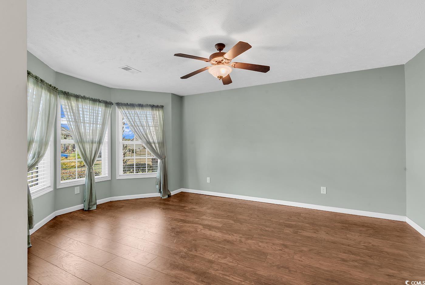 Empty room with wood finished floors, ceiling fan, and a textured ceiling