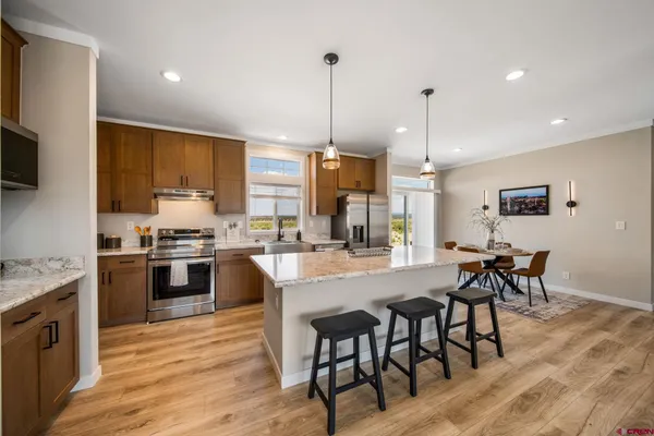 a kitchen with stainless steel appliances granite countertop a stove top oven a sink dishwasher a dining table and chairs with wooden floor