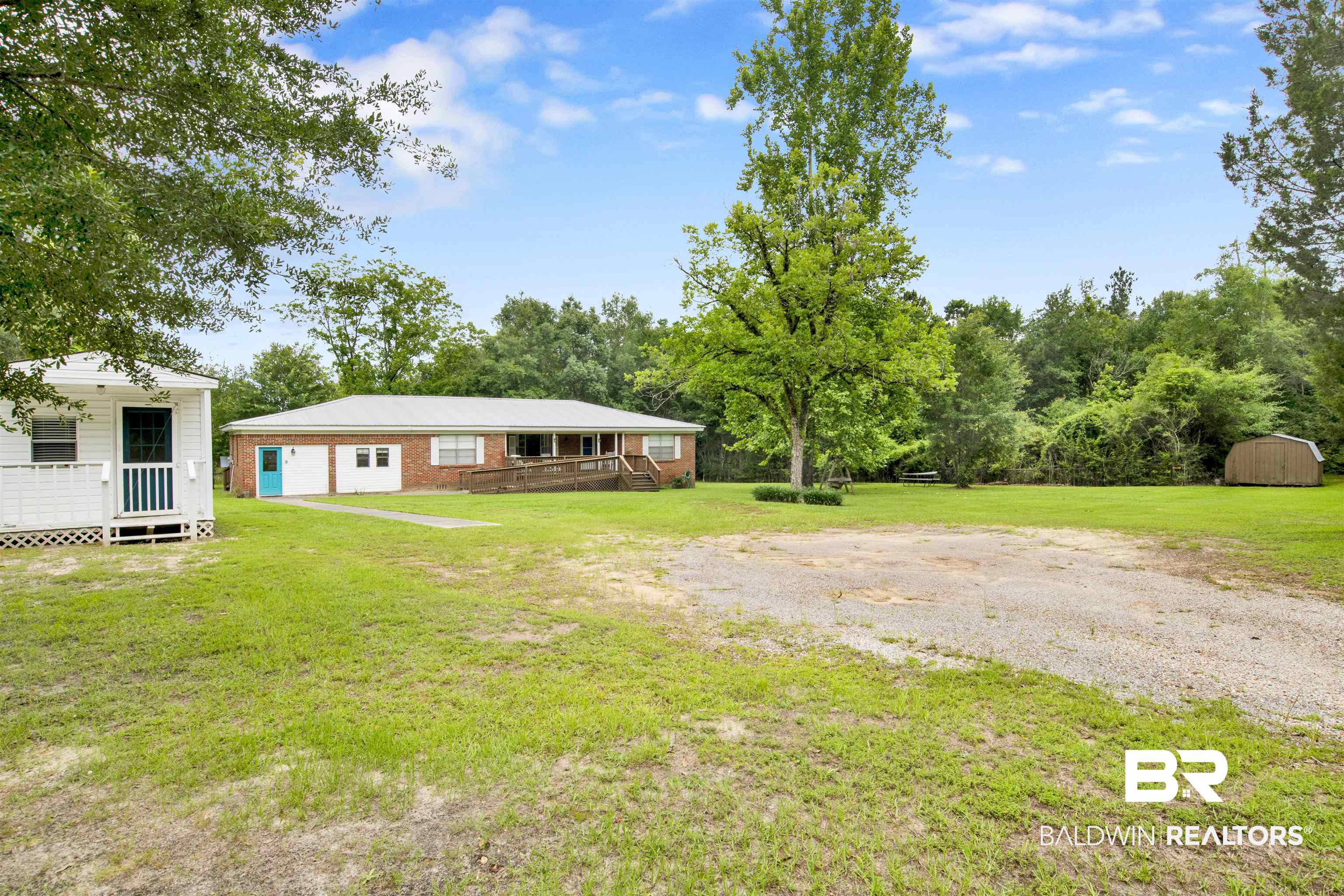 17714 Horseneck Road Bay Minette, AL 36507 - Photo 32 of 36 Expansive grassy lot featuring a brick-sided main residence with a metal roof and a separate white outbuilding with a porch