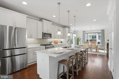 a kitchen with stainless steel appliances granite countertop a refrigerator a stove a sink a dining table and chairs with wooden floor