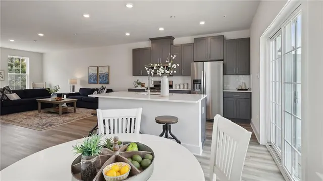 a living room with stainless steel appliances kitchen island granite countertop a refrigerator a sink a dining table and chairs with wooden floor