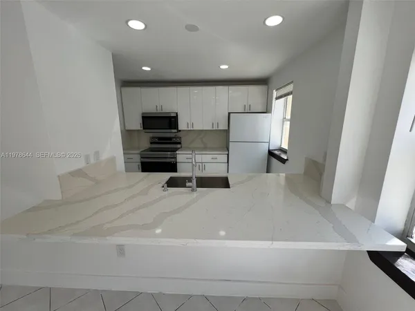 a large white kitchen with kitchen island a sink a stove and a refrigerator