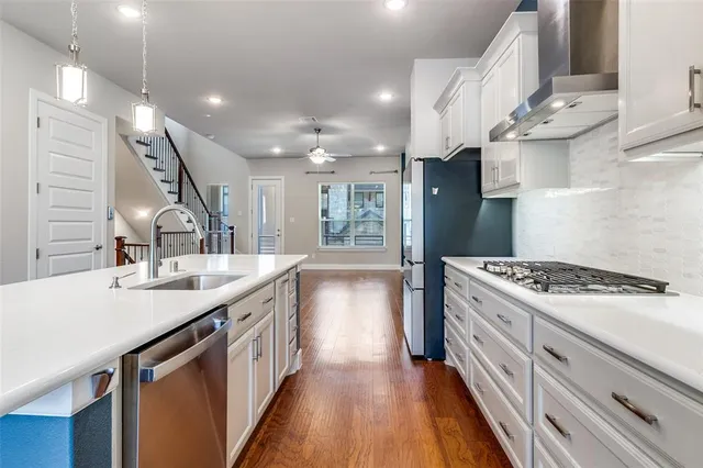 a large kitchen with stainless steel appliances granite countertop a large center island a stove a refrigerator cabinets and a wooden floor