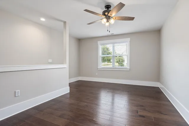 an empty room with wooden floor chandelier fan and windows