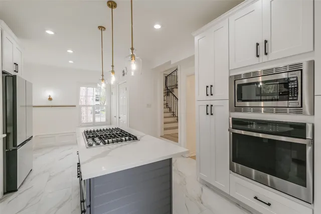 a kitchen with stainless steel appliances kitchen island granite countertop a stove a refrigerator and a oven with white cabinets