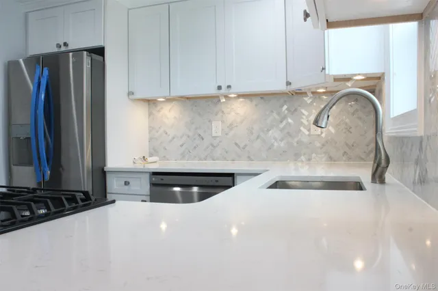 a kitchen with stainless steel appliances a stove a refrigerator a sink and white cabinets with wooden floor