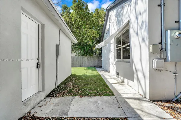a view of a white house with a small yard and large trees