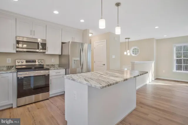 a kitchen with stainless steel appliances granite countertop a sink a stove a refrigerator and island with wooden floor