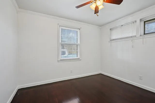 an empty room with wooden floor chandelier fan and windows