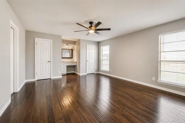 an empty room with wooden floor ceiling fan and windows