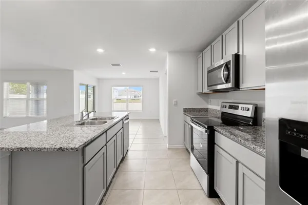 a large kitchen with stainless steel appliances granite countertop a stove a sink a refrigerator and white cabinets with wooden floor