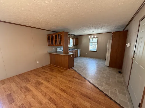 a view of kitchen and empty room with wooden floor and window