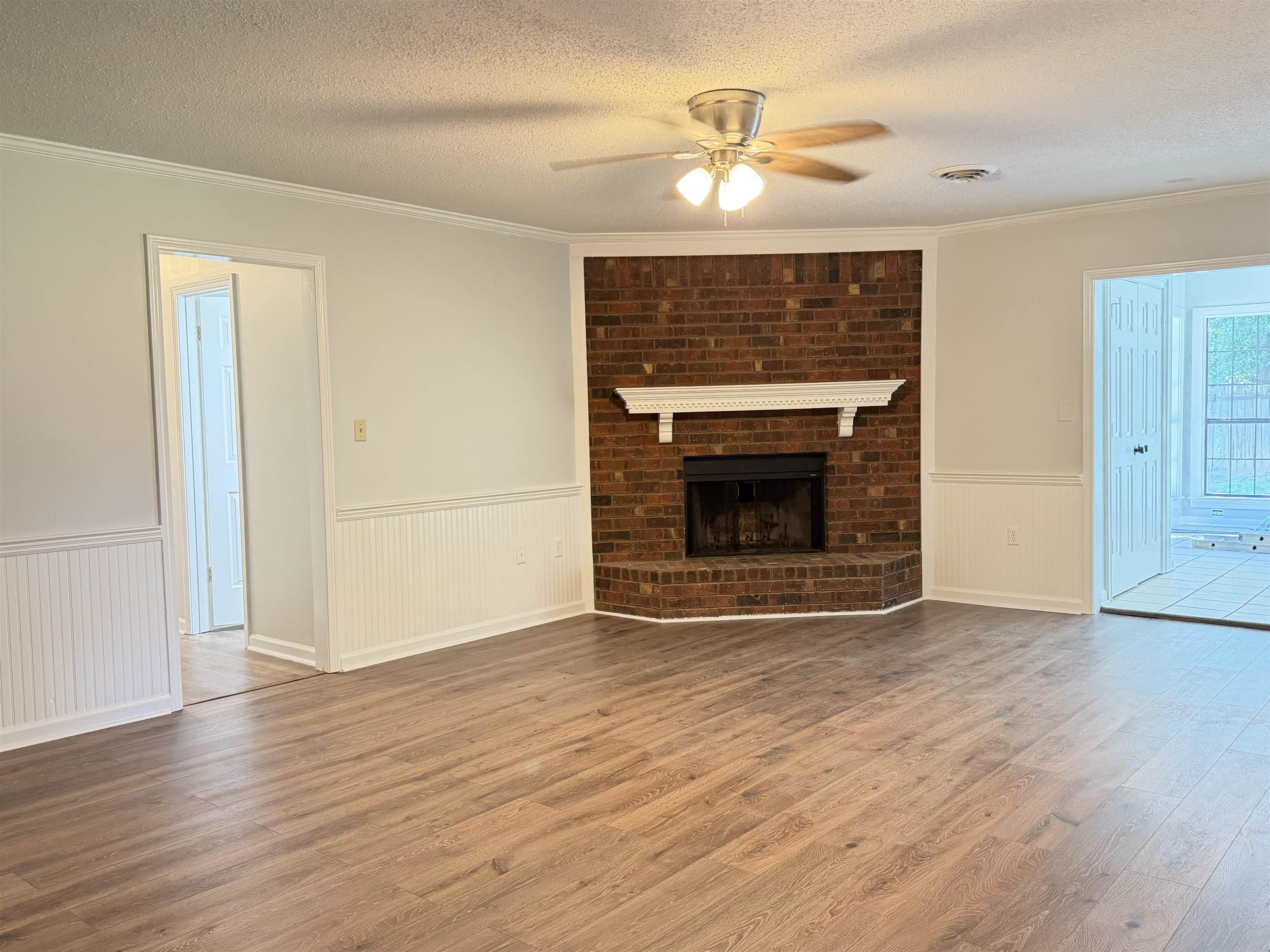 388 Park Hill Road Collierville, TN 38017 - Photo 10 of 19 Spacious interior featuring wood-finish flooring, a brick fireplace with a white mantel, white beadboard wainscoting, and a ceiling fan with integrated lighting