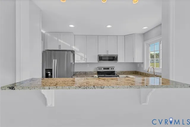 a kitchen with stainless steel appliances granite countertop a sink a stove a refrigerator a microwave and white cabinets