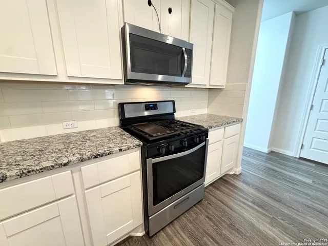 a kitchen with granite countertop wooden cabinets stainless steel appliances and a wooden floor