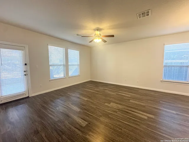 an empty room with wooden floor chandelier fan and windows