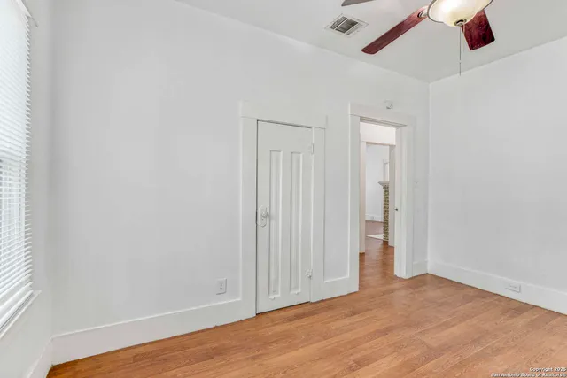 an empty room with wooden floor ceiling fan and window