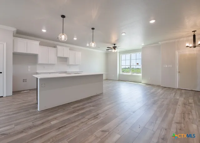 a view of an empty room and kitchen with wooden floor