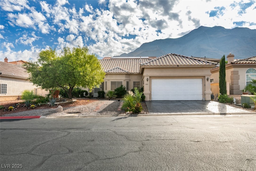 Mediterranean / spanish-style house with stucco siding, a tiled roof, driveway, an attached garage, and a mountain view