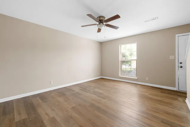 an empty room with wooden floor fan and windows