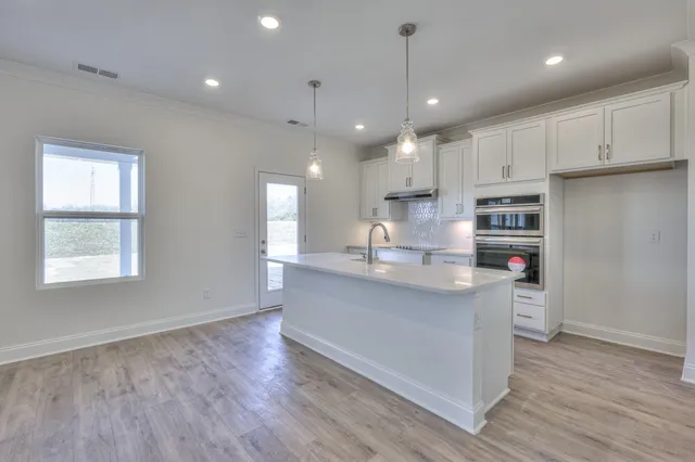 a kitchen with stainless steel appliances granite countertop a sink a stove a refrigerator and white cabinets with wooden floor