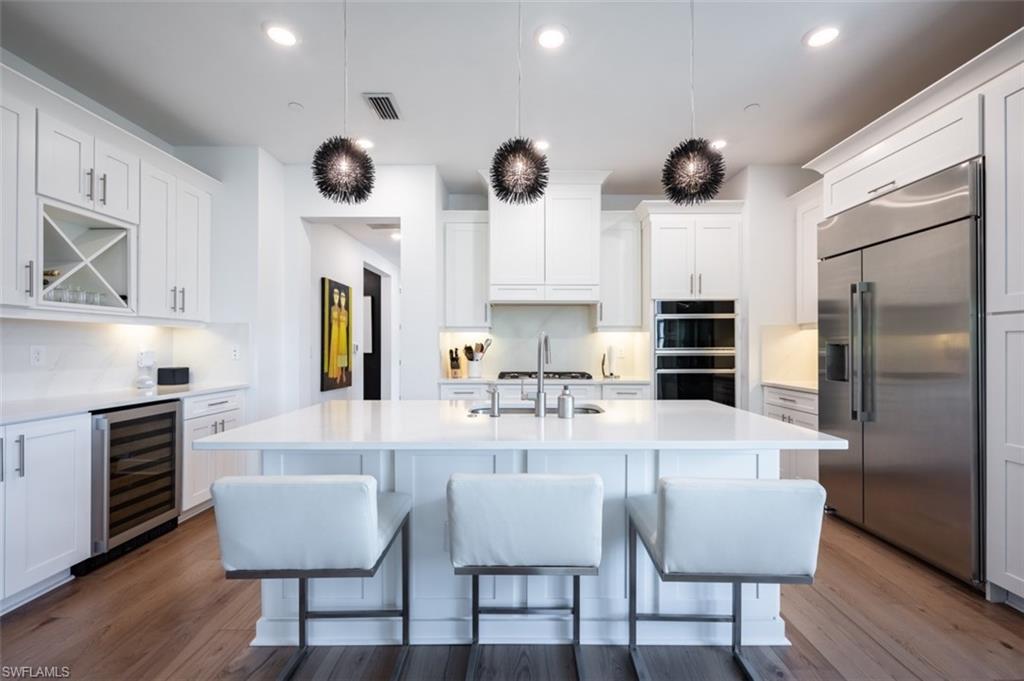 16360 Viansa Way, Unit 8201 Naples, FL 34110 - Photo 2 of 35 a kitchen with stainless steel appliances granite countertop a stove a refrigerator a dining table and chairs with wooden floor