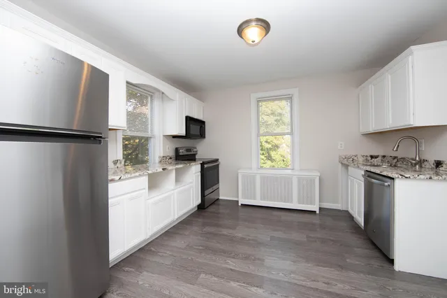 a kitchen with a refrigerator a stove top oven a white cabinets and wooden floor