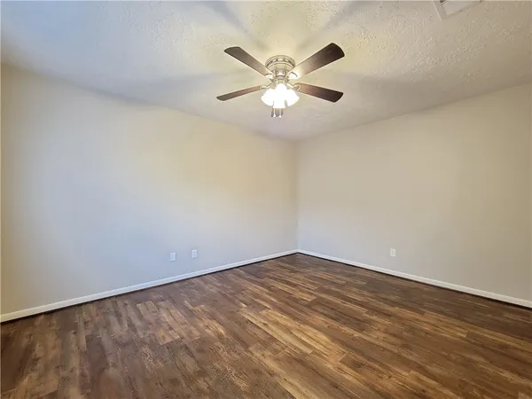 a view of an empty room with wooden floor and a ceiling fan