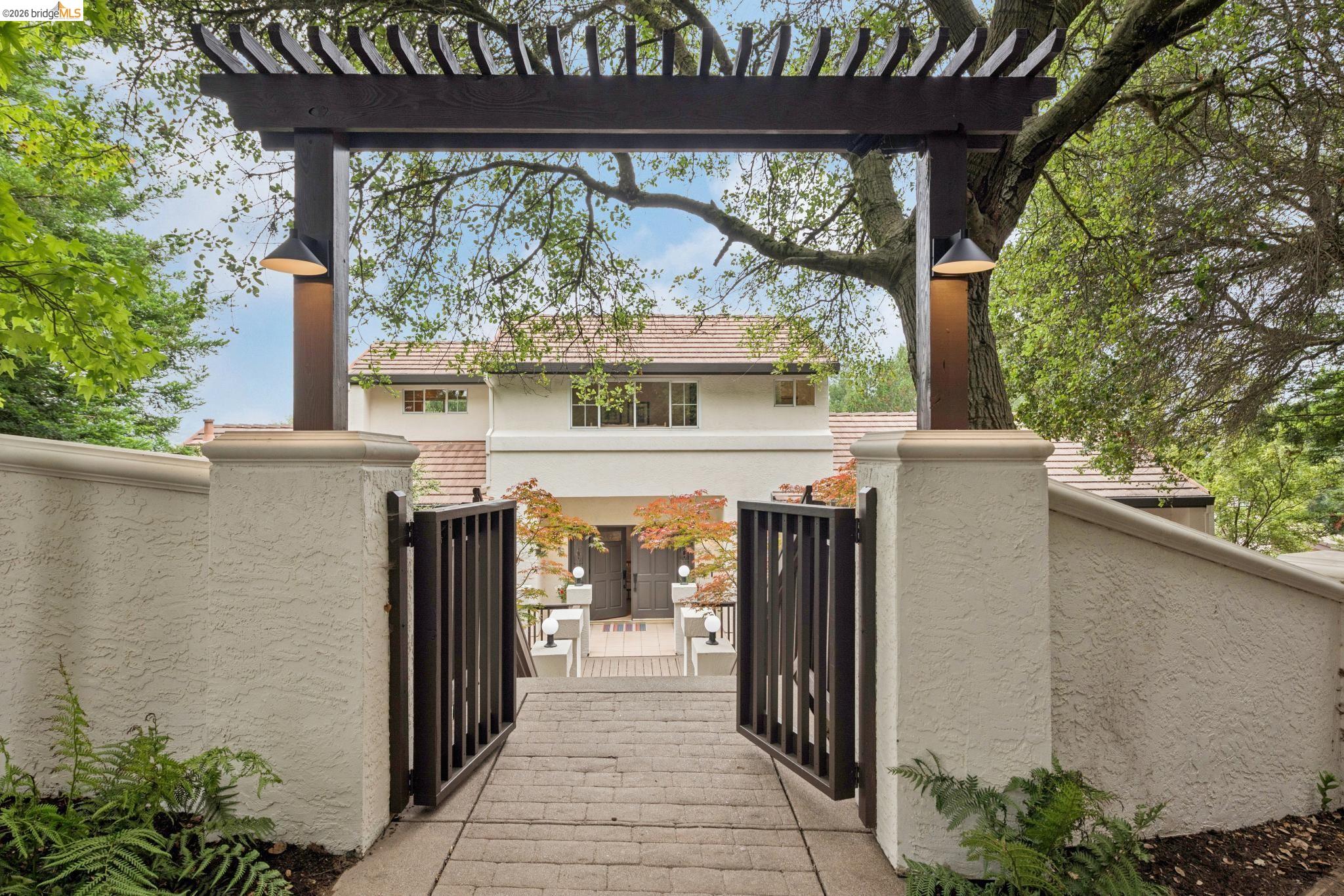 1325 Drury Road Berkeley, CA 94705 - Photo 7 of 71 Custom entry gate with decorative wood pergola and integrated lighting, leading to a multi-story residence with a red tile roof and double front doors