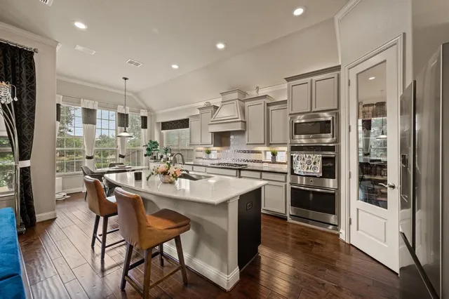 a kitchen with stainless steel appliances kitchen island granite countertop a refrigerator a stove top oven a sink dishwasher and white cabinets with wooden floor