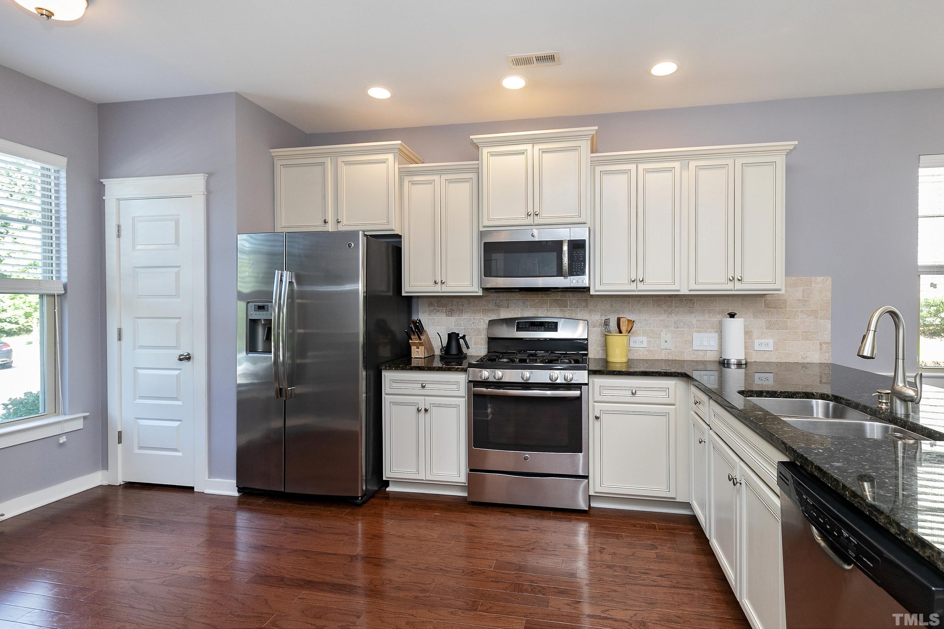 7906 Allscott Way Raleigh, NC 27612 - Photo 4 of 30 a kitchen with stainless steel appliances granite countertop white cabinets a refrigerator a sink a stove a microwave and wooden floors