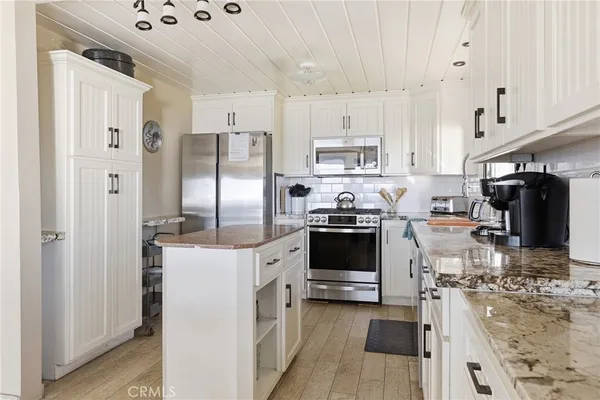 a kitchen with stainless steel appliances kitchen island granite countertop a refrigerator a stove a sink and white cabinets with wooden floor