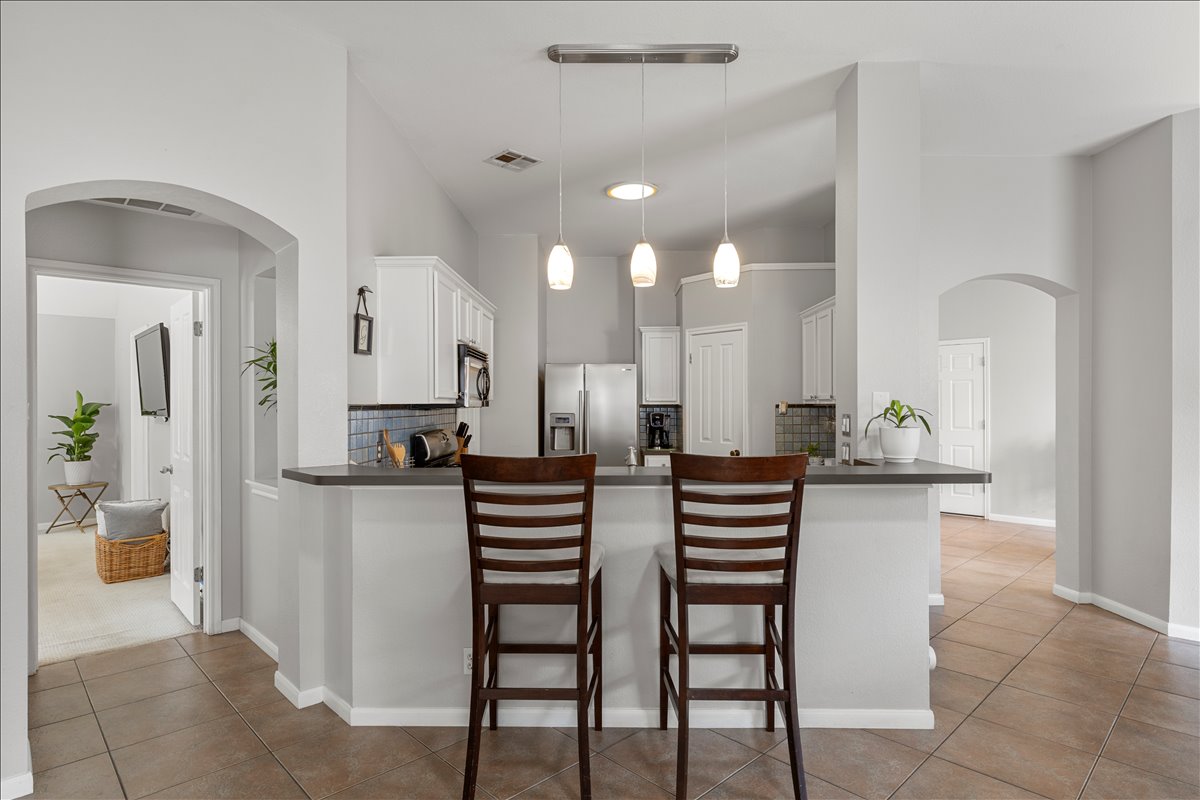 9012 Meacham Way Austin, TX 78749 - Photo 11 of 34 Open-concept kitchen featuring a breakfast bar with stone-finish countertop, white cabinetry, integrated stainless steel appliances, a tiled backsplash, and recessed lighting
