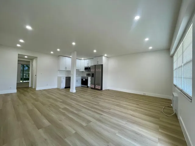 a view of an empty room with wooden floor and kitchen