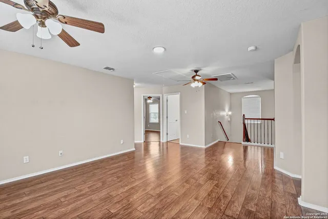 a view of an empty room with wooden floor and a ceiling fan
