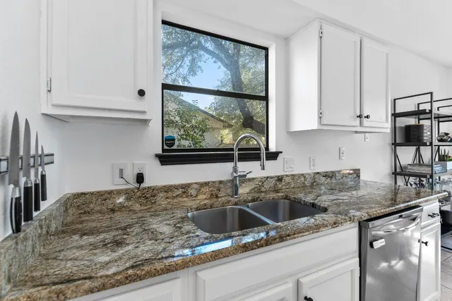 a kitchen with granite countertop a sink window and cabinets