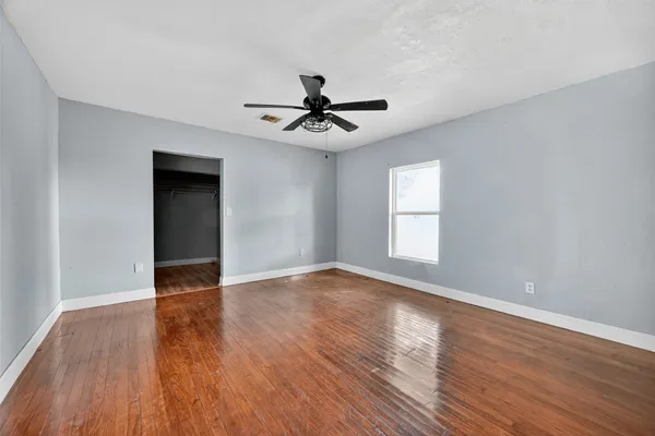 a view of empty room with wooden floor and fan