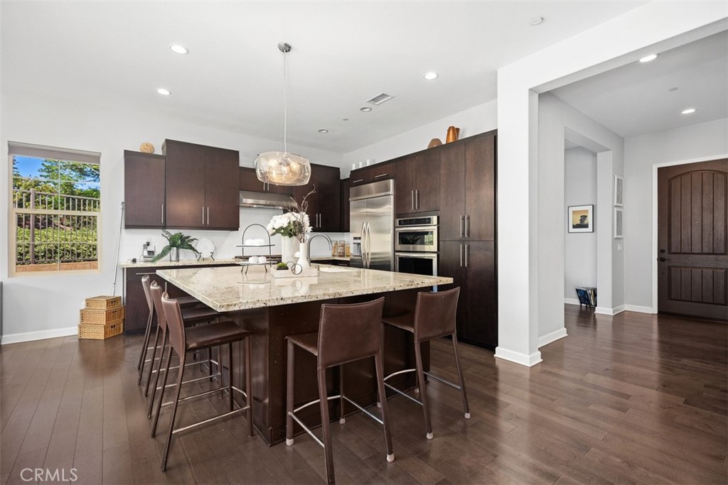 3 Planeo Rancho Mission Viejo, CA 92694 - Photo 8 of 37 a kitchen with stainless steel appliances kitchen island granite countertop a refrigerator a stove a microwave oven with a dining table and chairs with wooden floor