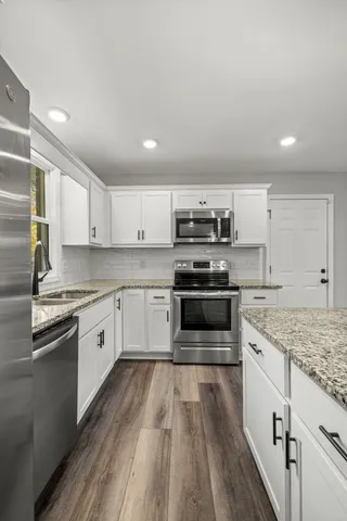 a kitchen with stainless steel appliances granite countertop a stove a sink and white cabinets