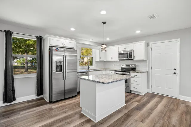 a kitchen with stainless steel appliances granite countertop a refrigerator a sink dishwasher a stove and white cabinets with wooden floor