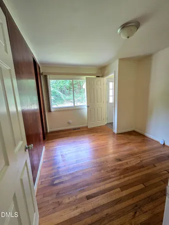 a view of an empty room with wooden floor and a window