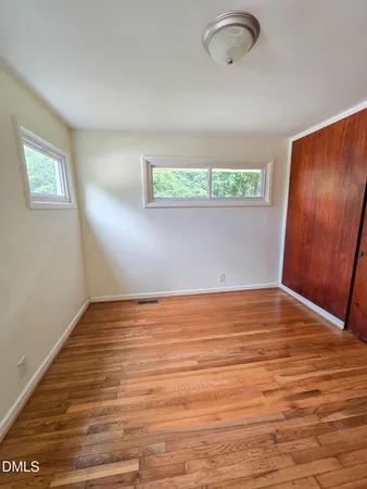 a view of an empty room with wooden floor and fan
