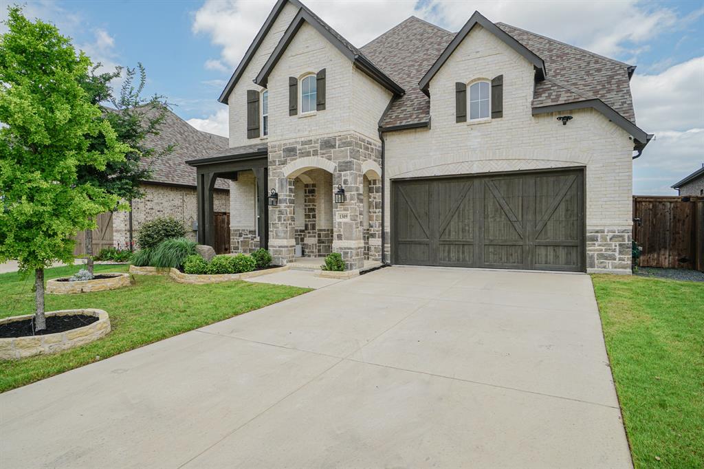 1309 Old Rocksprings Pass Mansfield, TX 76063 - Photo 33 of 36 Two-story exterior featuring a light-colored brick and stone facade, dark wood-finish garage door, arched entry, and dark trim details