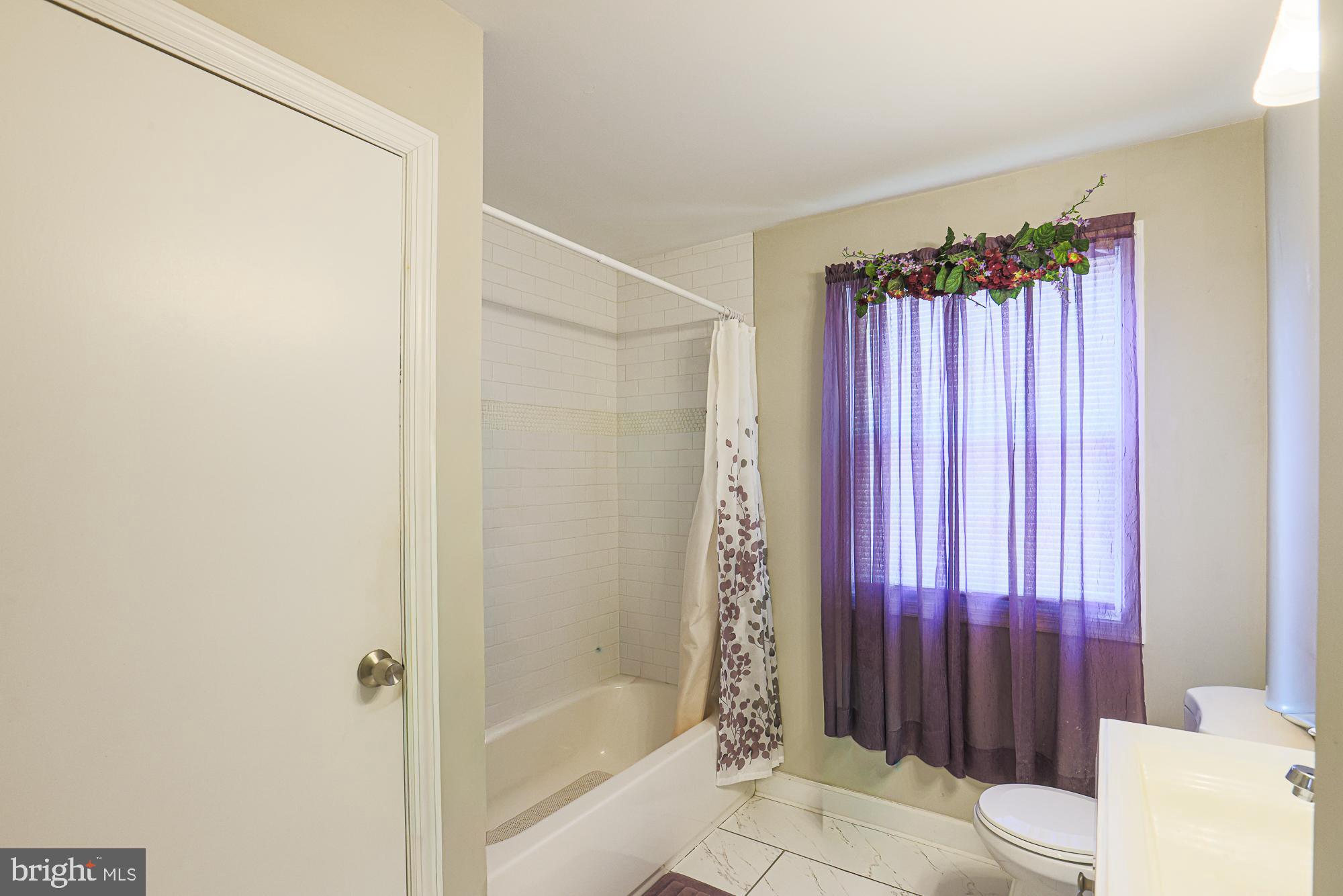 7933 34th Street Rosedale, MD 21237 - Photo 18 of 32 a bathroom with a shower curtain a mirror and a toilet