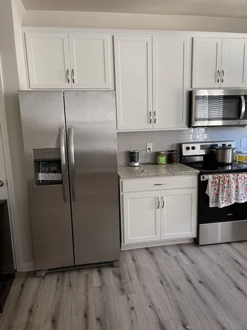 a kitchen with stainless steel appliances granite countertop a refrigerator a stove a sink and white cabinets with wooden floor