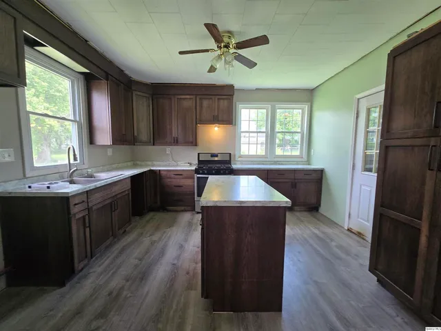 a kitchen with kitchen island granite countertop wooden floors stainless steel appliances a sink and a window