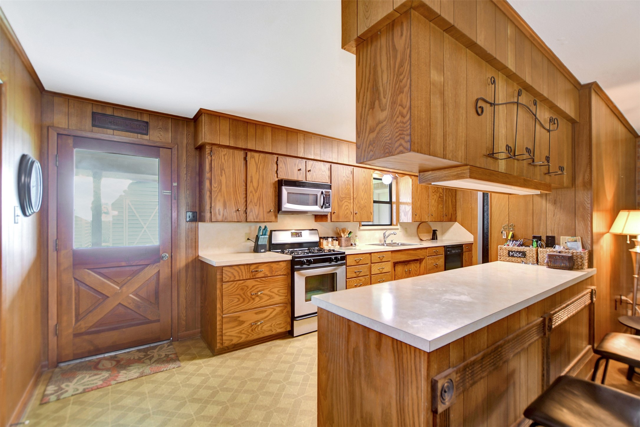 341 South S Loop Bellville, TX 77418 - Photo 10 of 33 This kitchen features warm wood paneling, a modern stainless steel stove and microwave, ample cabinetry, and a cozy breakfast bar with seating. The layout is functional and inviting, perfect for both cooking and socializing.