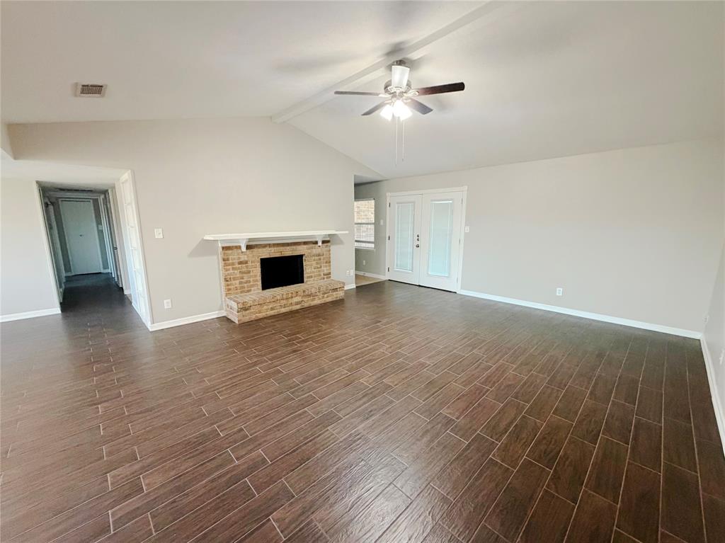 8601 Woodside Road Rowlett, TX 75088 - Photo 5 of 22 Spacious room featuring vaulted ceilings, wood-finish flooring, a brick fireplace, and double French doors