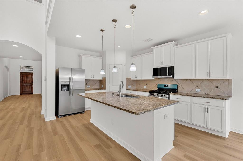 174 Hampton Drive Fate, TX 75087 - Photo 8 of 40 a kitchen with stainless steel appliances granite countertop a stove top oven a refrigerator a sink and white cabinets with wooden floor